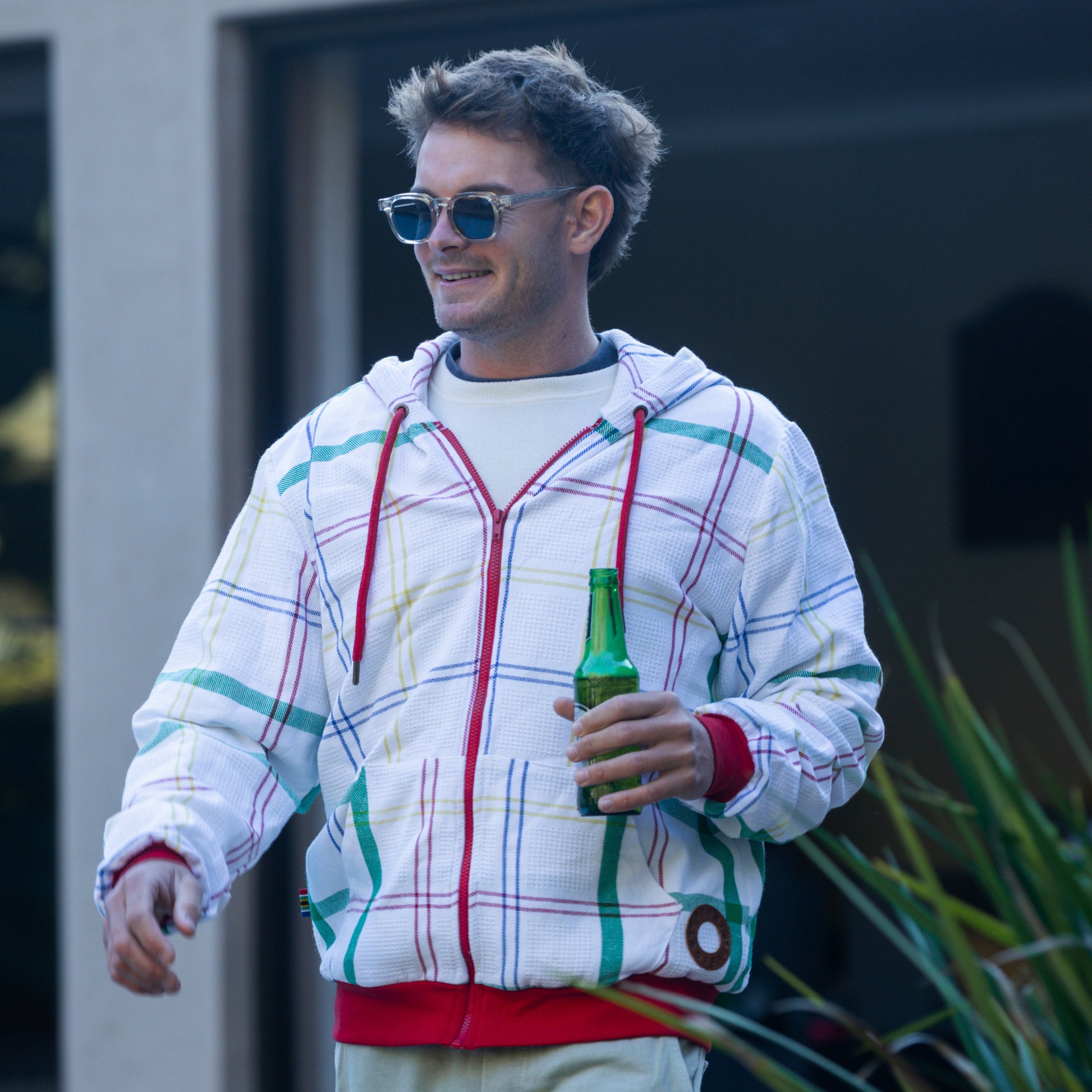 Man wearing a colorful hoodie made from dishcloth holding a beer bottle outdoors.