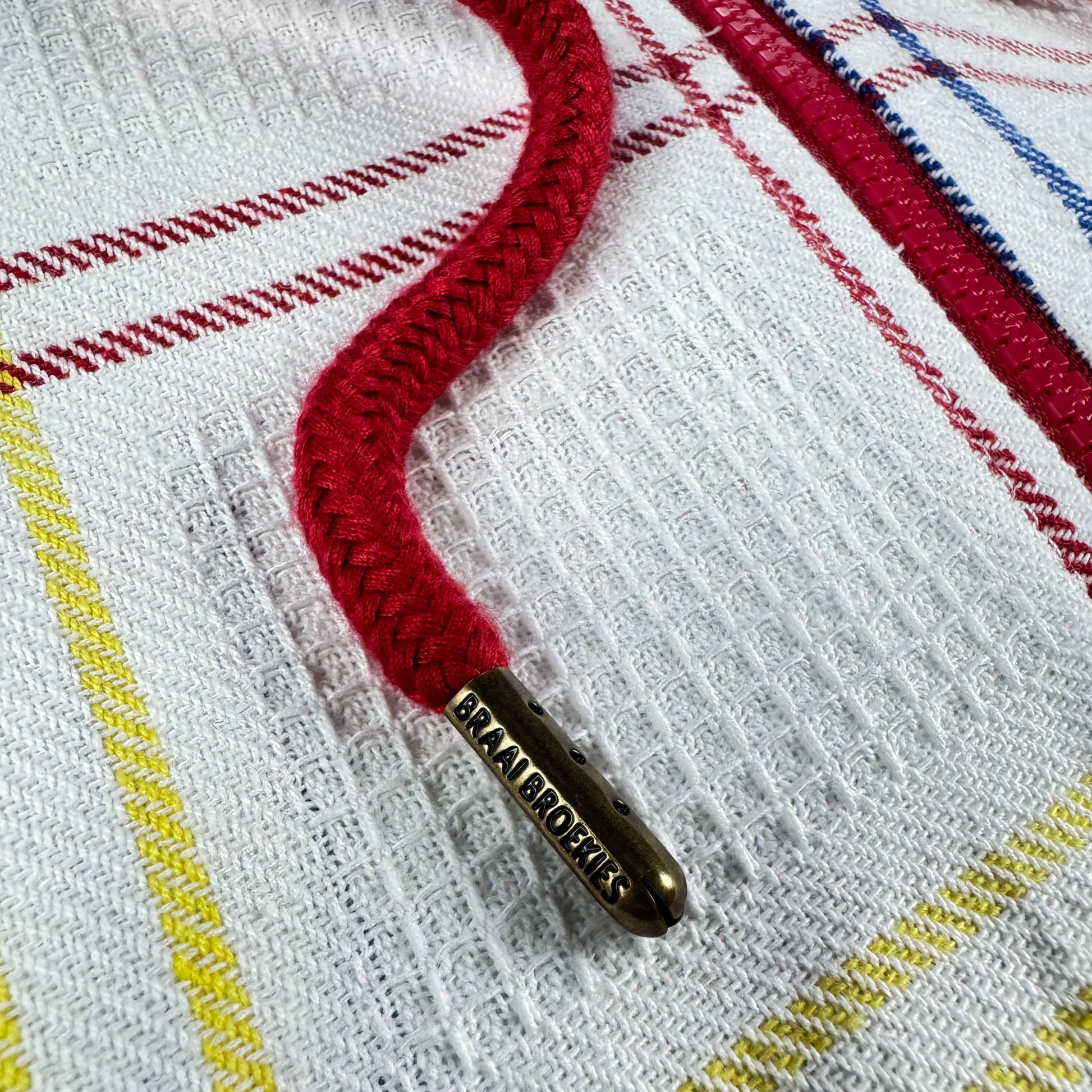 Close-up of a red drawchord with a branded chord end that says braai broekies. Dishcloth background